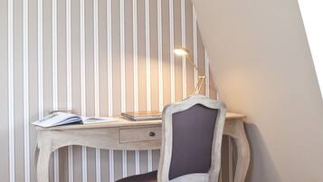 A corner room with a sloped ceiling, a desk with a lamp, and a chair.