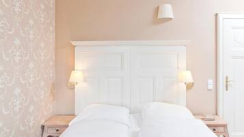 Habitación de hotel con cama doble, dos mesitas de noche con lámparas, una puerta blanca y un papel tapiz estampado en una pared.