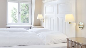 Un dormitorio con una cama grande, un aparador, dos lámparas de pared y una ventana con vistas a árboles.