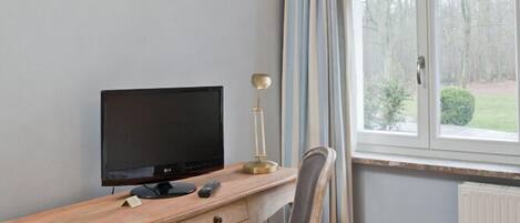 Una habitación con un escritorio de madera, una silla, un televisor y una ventana con cortinas.