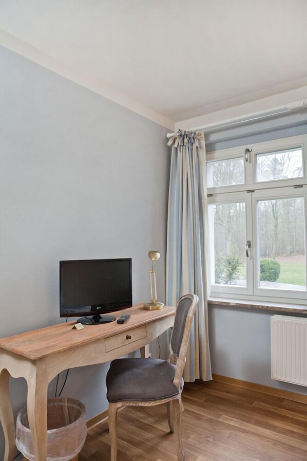 A room with a wooden desk, a chair, a television, and a window with curtains.