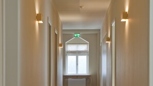 Un pasillo largo y estrecho con pisos alfombrados y paredes, que conduce a una habitación con ventana y radiador.