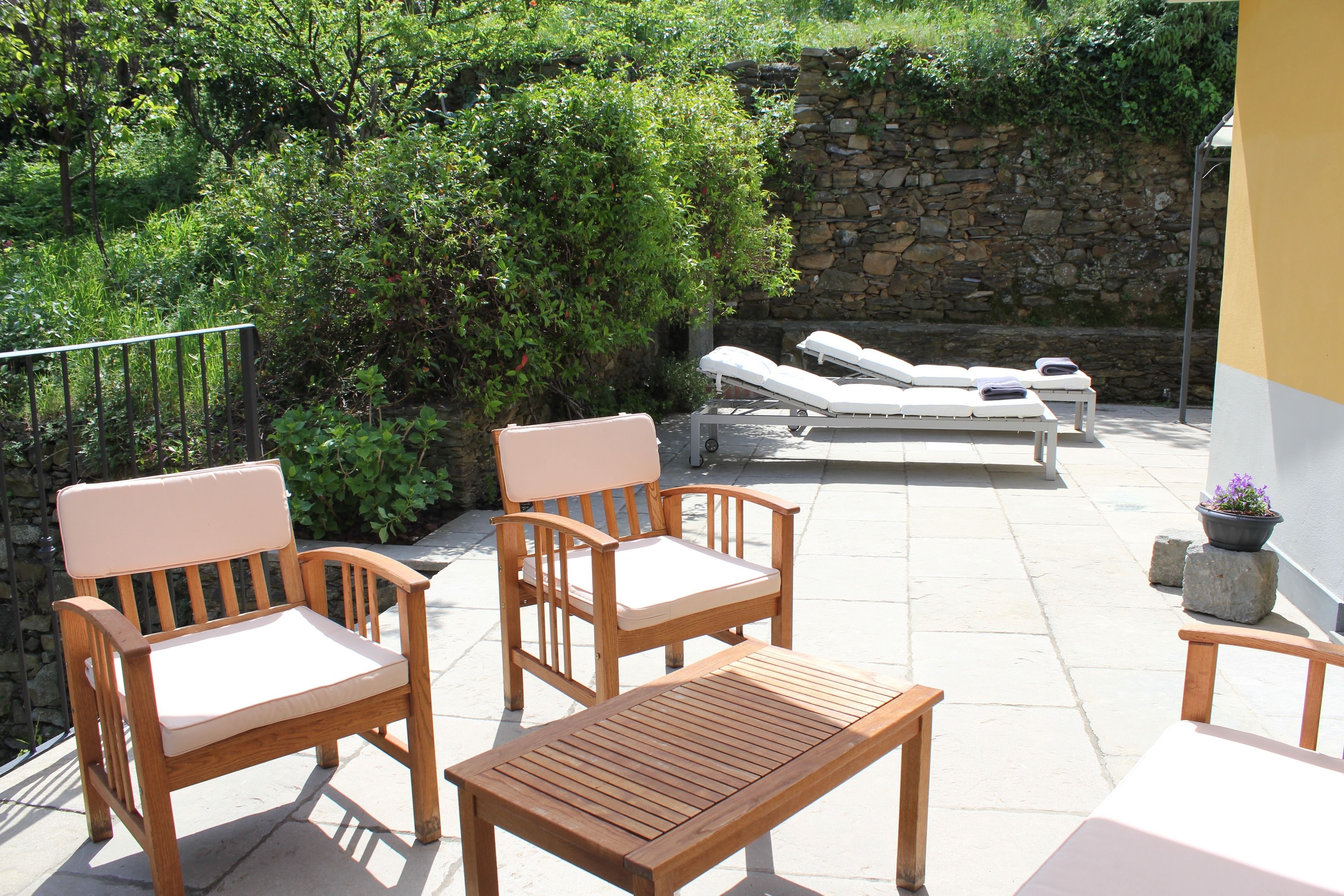 A patio with wooden furniture, including chairs and a table, and a lounge area with sun loungers.