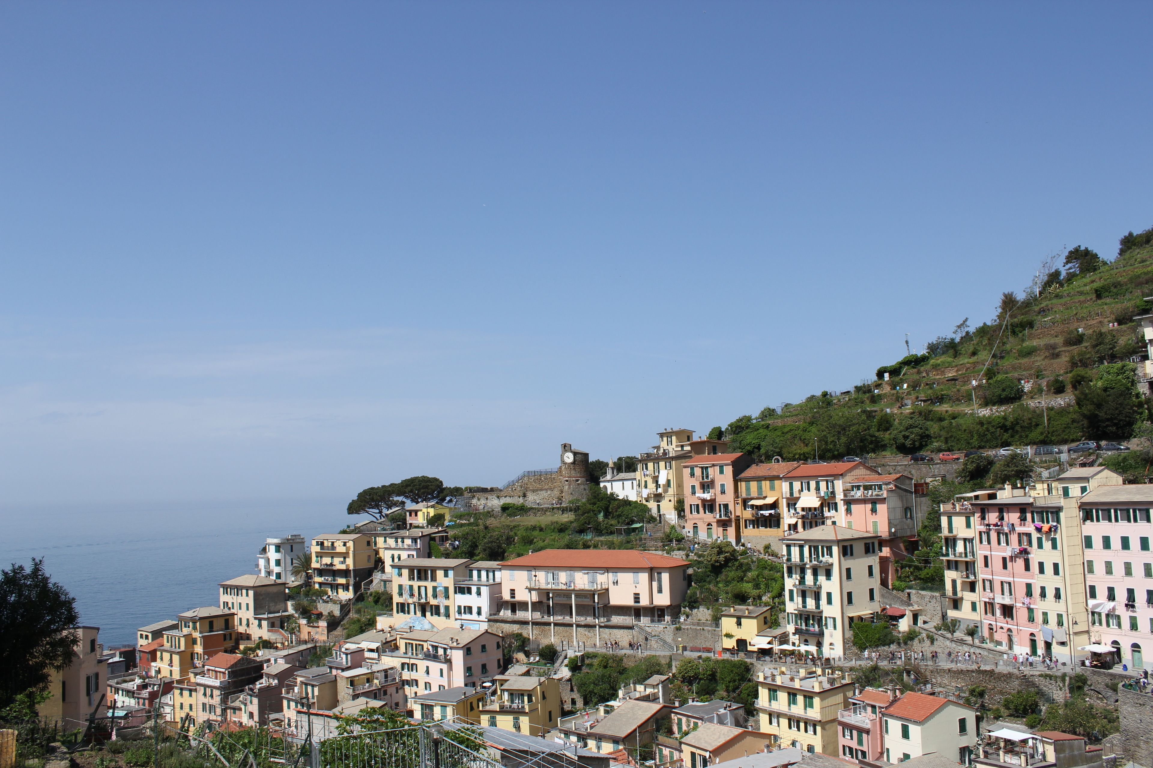 Une ville côtière aux bâtiments aux couleurs vives, dotée d’une tour imposante et bordée d’une colline verdoyante.
