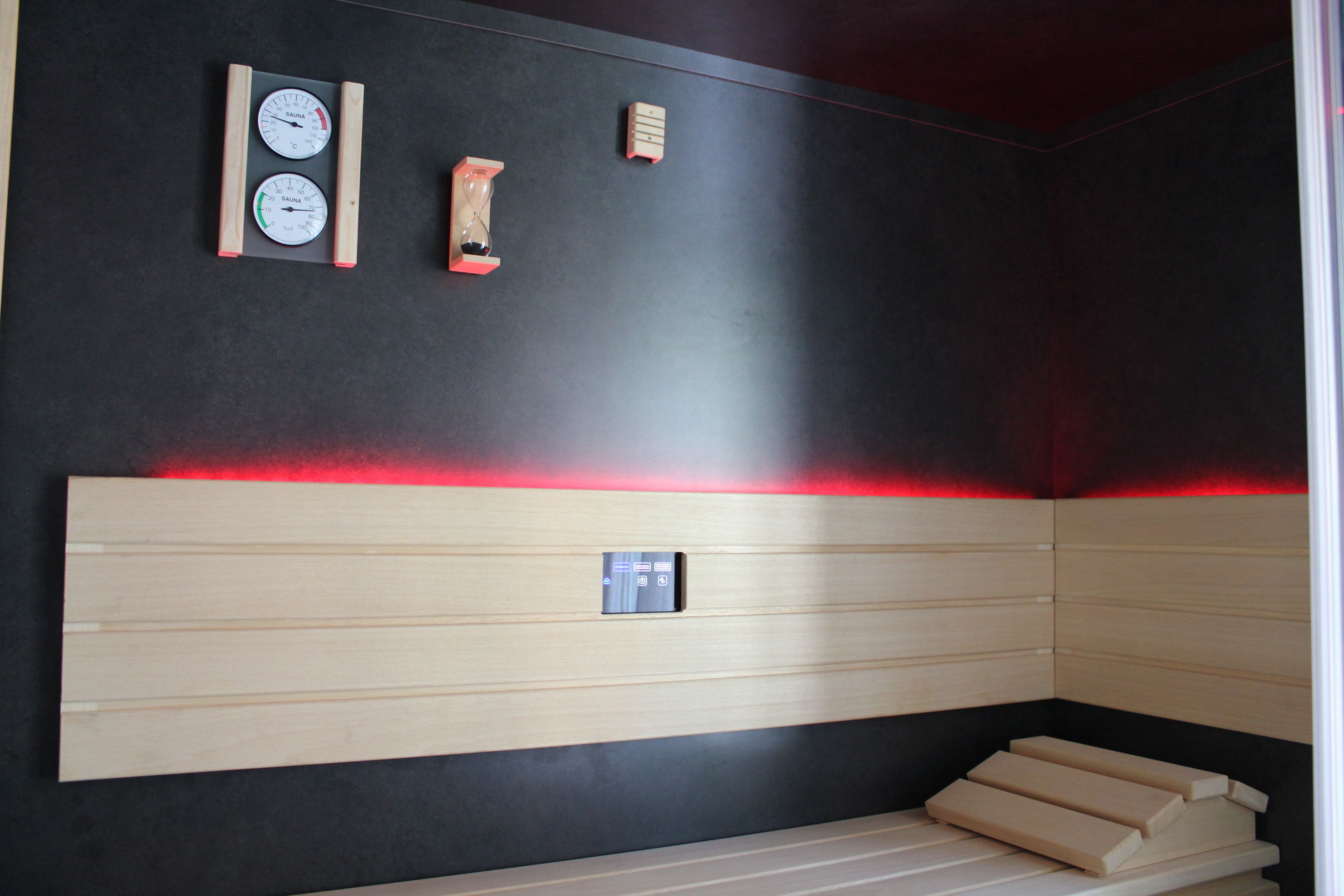 Una sauna con panche in legno, un pannello di controllo e due termometri fissati alla parete.