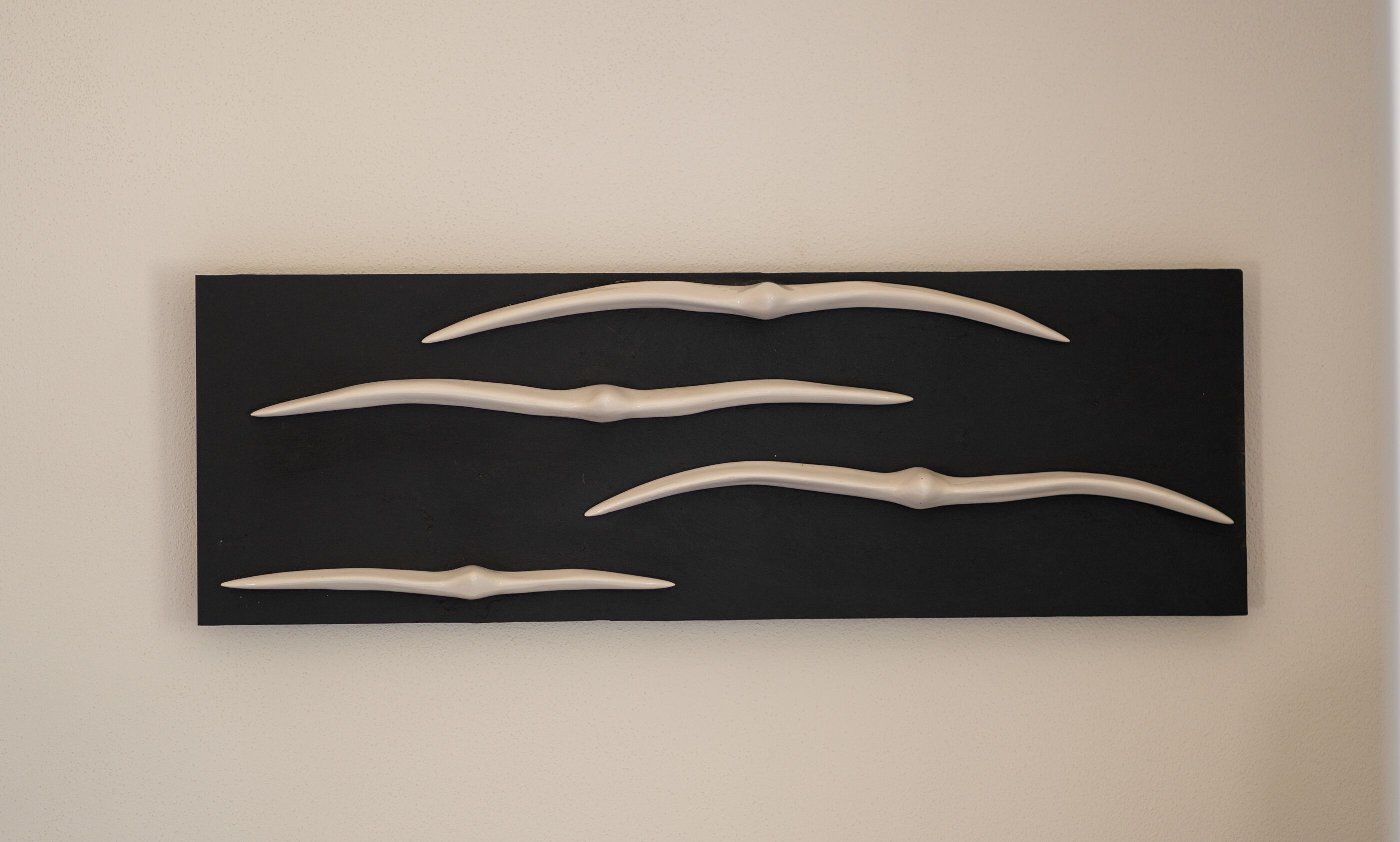 Un objeto rectangular negro con cuatro formas blancas y curvas sobre una pared color beige.