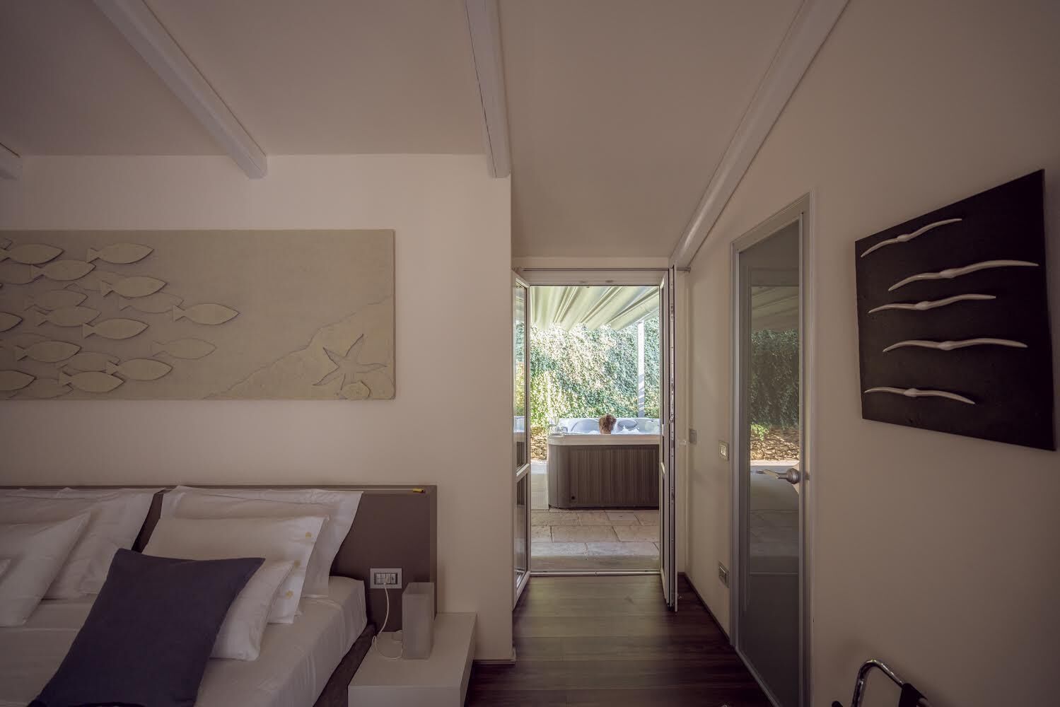 A bedroom with a bed, a nightstand, and a view of a hot tub outside.