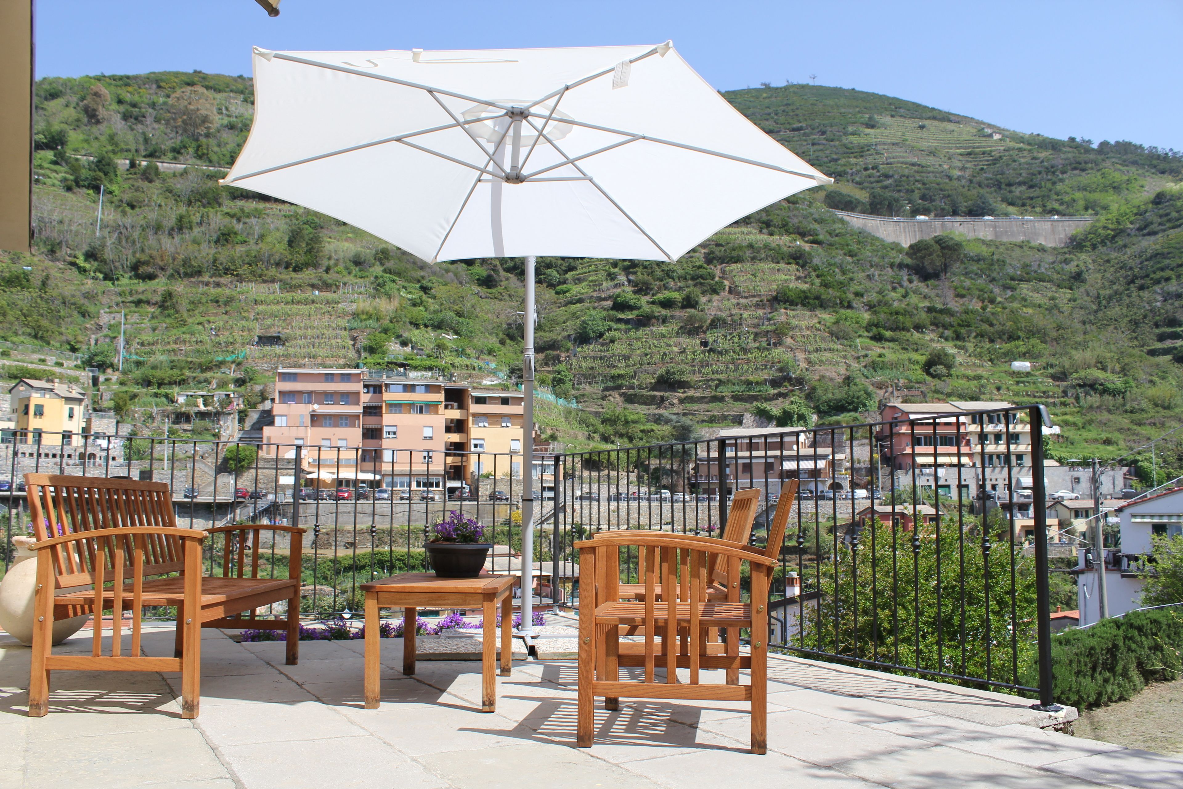 Un balcon avec des chaises en bois, une table et un parasol blanc.