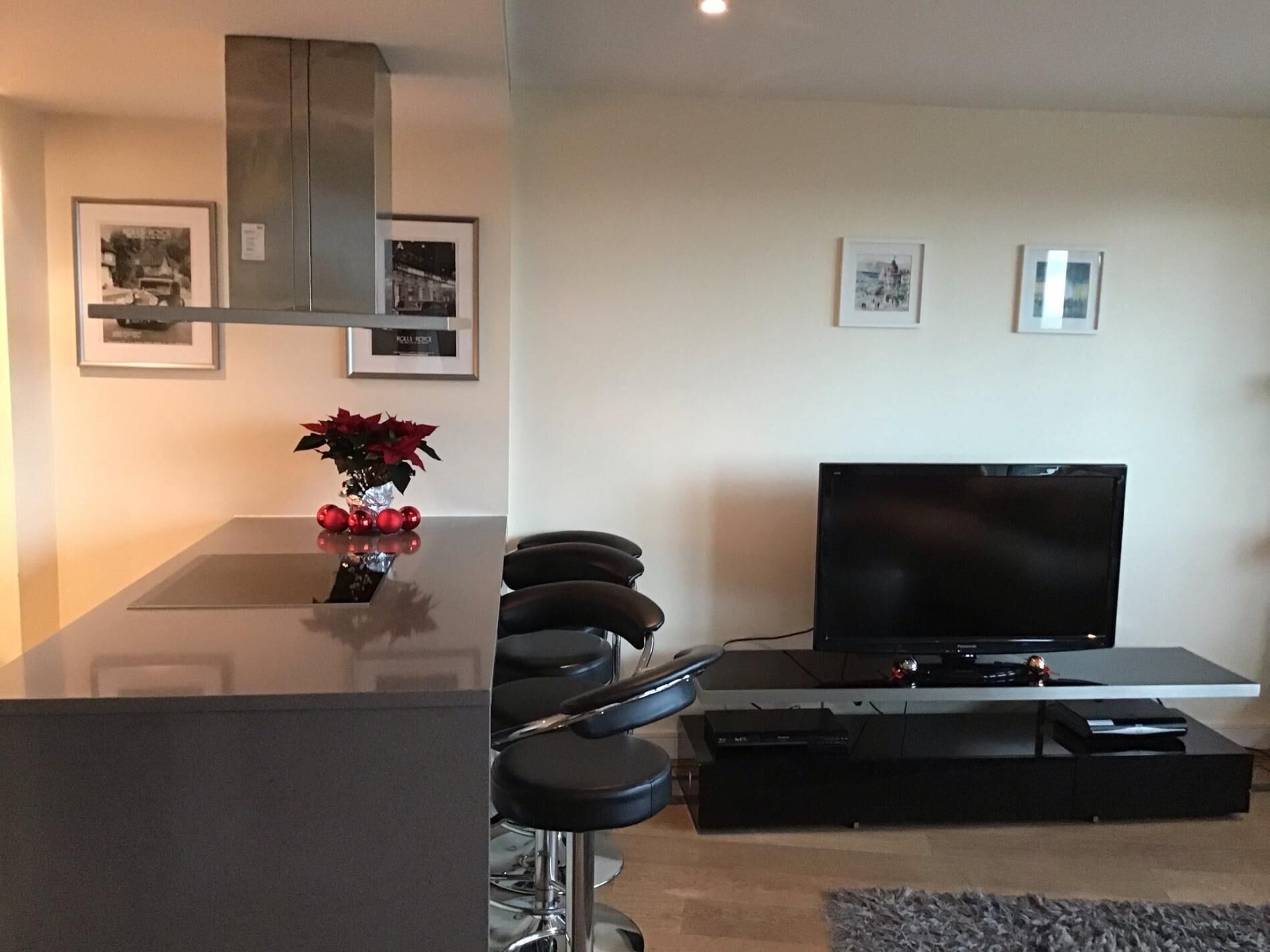 Een moderne woonkamer met een flatscreen televisie, een eettafel met stoelen, en een keuken met een rvs afzuigkap.