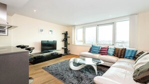 Een moderne woonkamer met een bank, een glazen salontafel, een flatscreen televisie en een keuken met een fornuis.