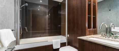 A modern bathroom with a glass-enclosed shower, a wooden vanity with a mirror, and a white toilet.