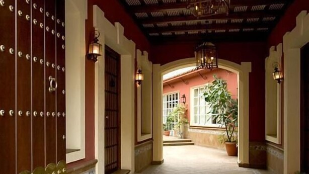 Un pasillo con suelo de baldosas, una puerta de madera con remaches metálicos y un farol colgante.