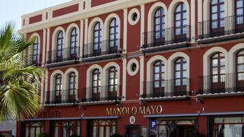 Experience the classic charm of Manolo Mayo Hotel, featuring a symmetrical facade, multiple balconies, and a restaurant with outdoor seating.