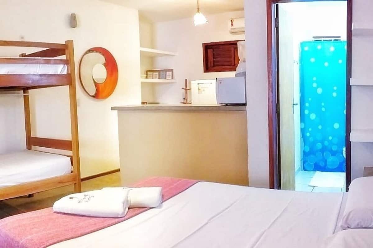 Ein Zimmer mit Etagenbetten, einem Schreibtisch, einem Stuhl, einer kleinen Küchenzeile und einem Badezimmer mit Duschvorhang.