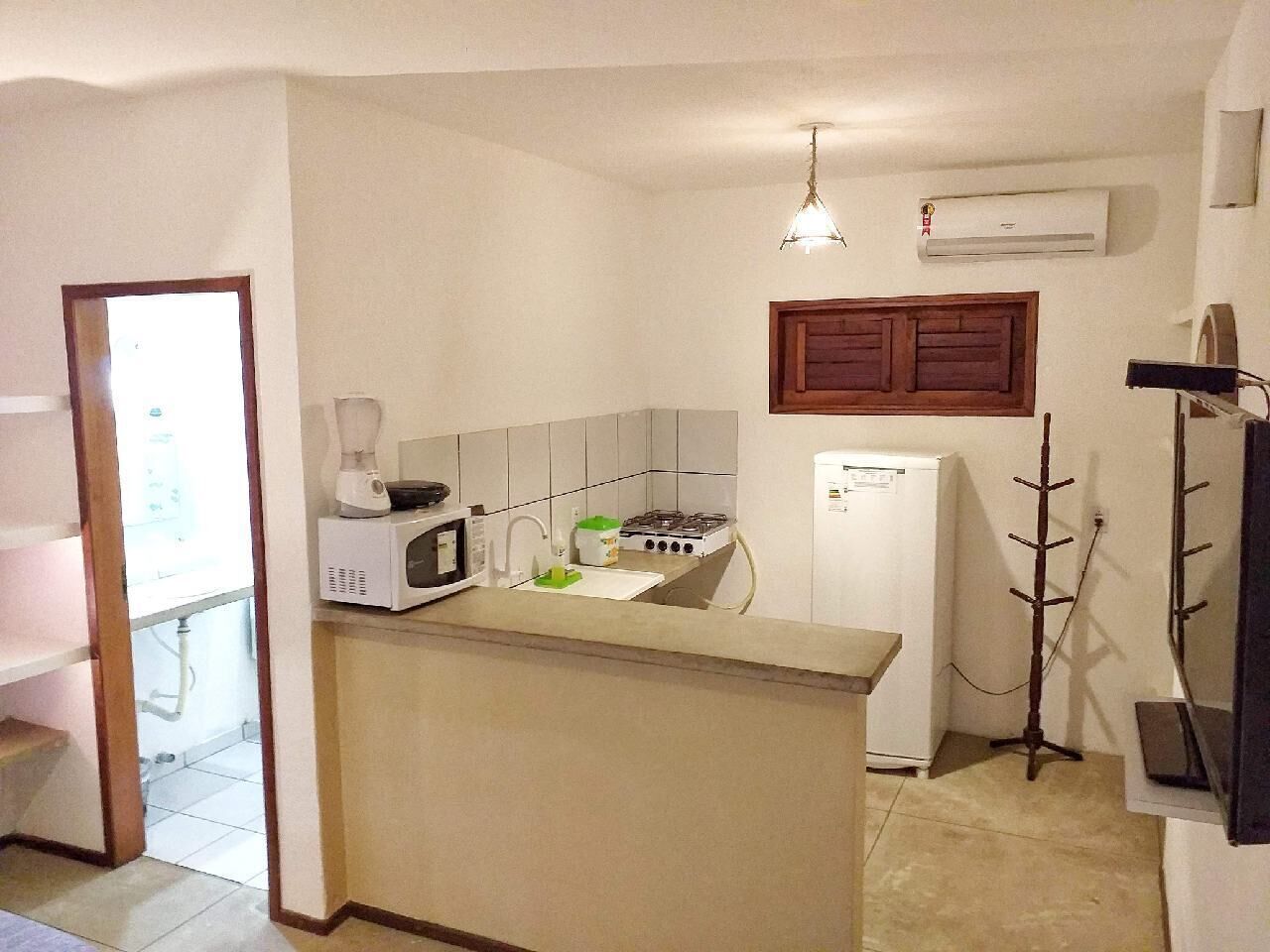 Una cocina compacta con microondas, estufa y pileta. Hay un refrigerador y un armario de madera sobre la estufa.