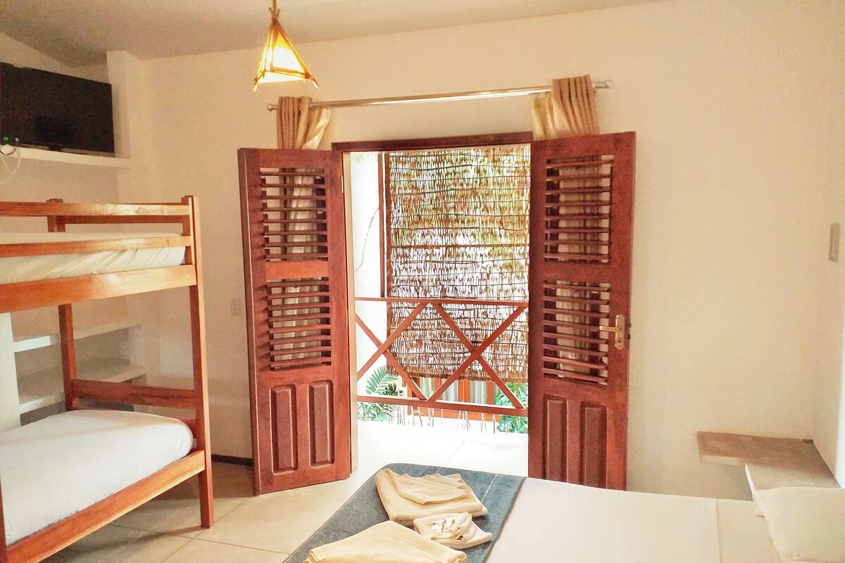 Ein Zimmer mit Etagenbetten, einem Bett, einem Tisch mit gefalteter Kleidung und Blick durch eine Holztür.