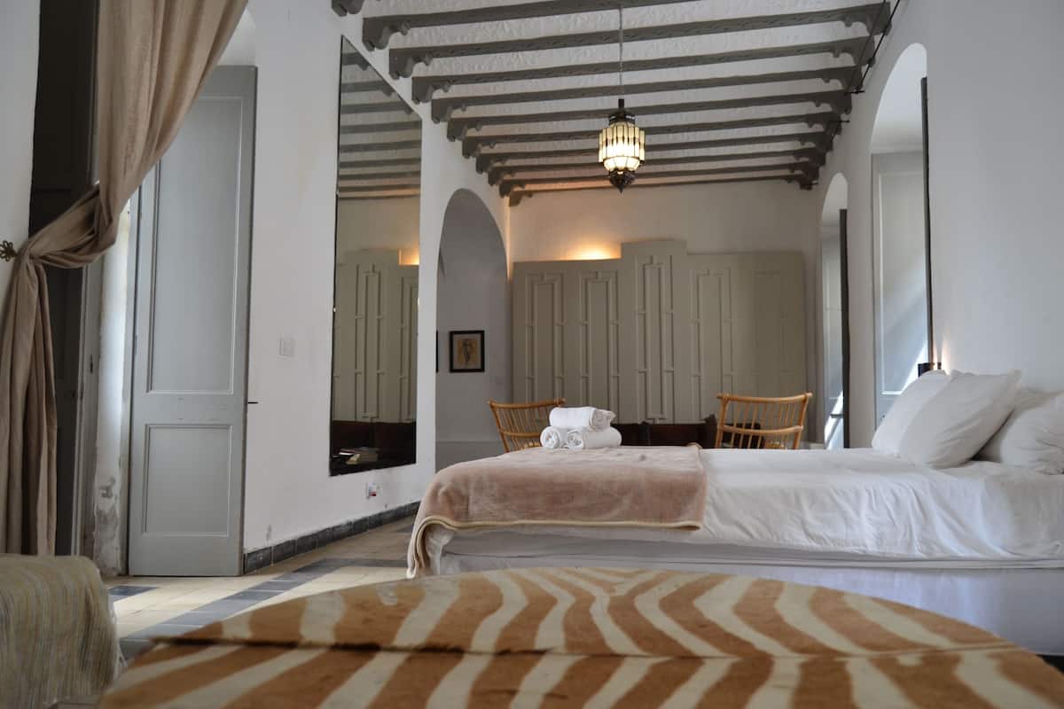 A bedroom with a bed, a chair, a table with a towel, and a hanging light fixture.