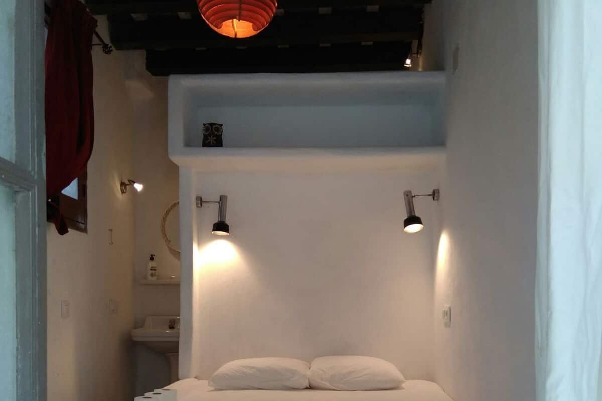 A small, cozy bedroom with a single bed, two bedside lamps, and a red hanging light fixture.