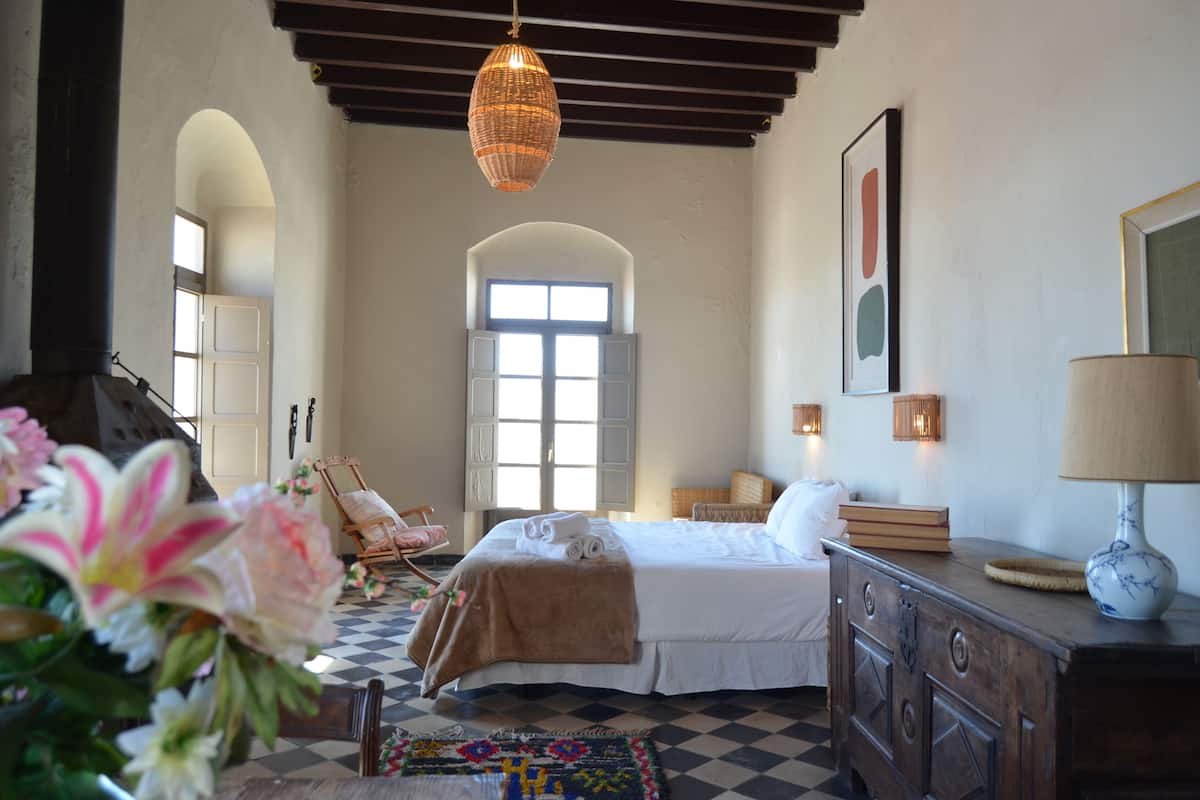 A bedroom with a bed, a dresser, a lamp, a chair, and a window.