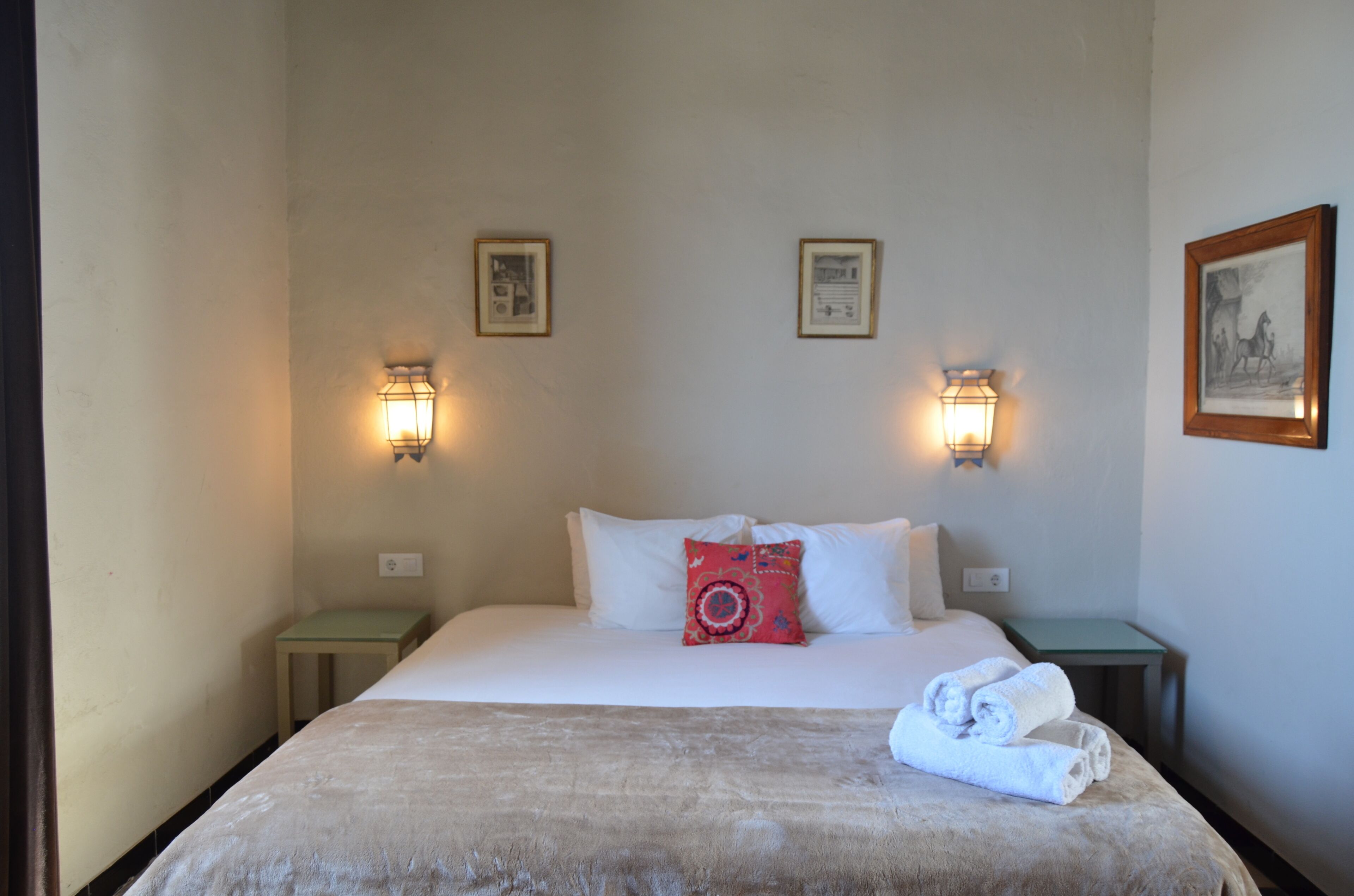 A hotel room with a bed, two bedside tables, two wall-mounted lamps, and two framed pictures on the wall.