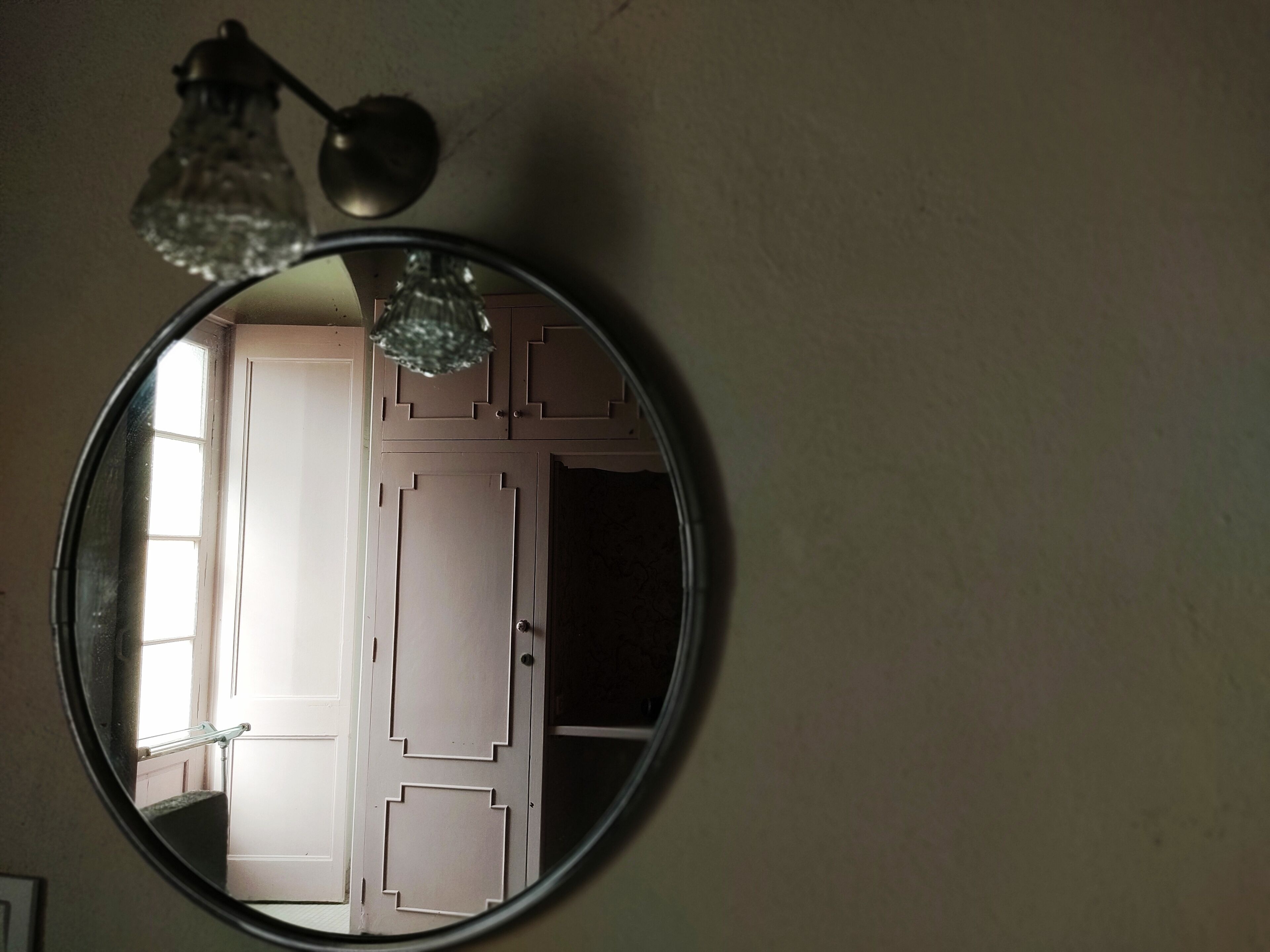 A round mirror with a geometric wall design and a hanging light fixture.