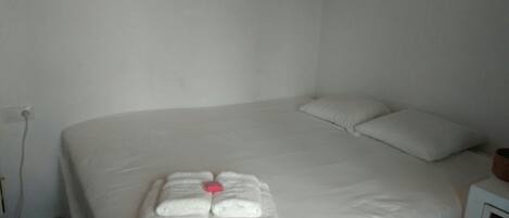 Una cama bien hecha con sábanas blancas y un juego de toallas dispuestas sobre ella.