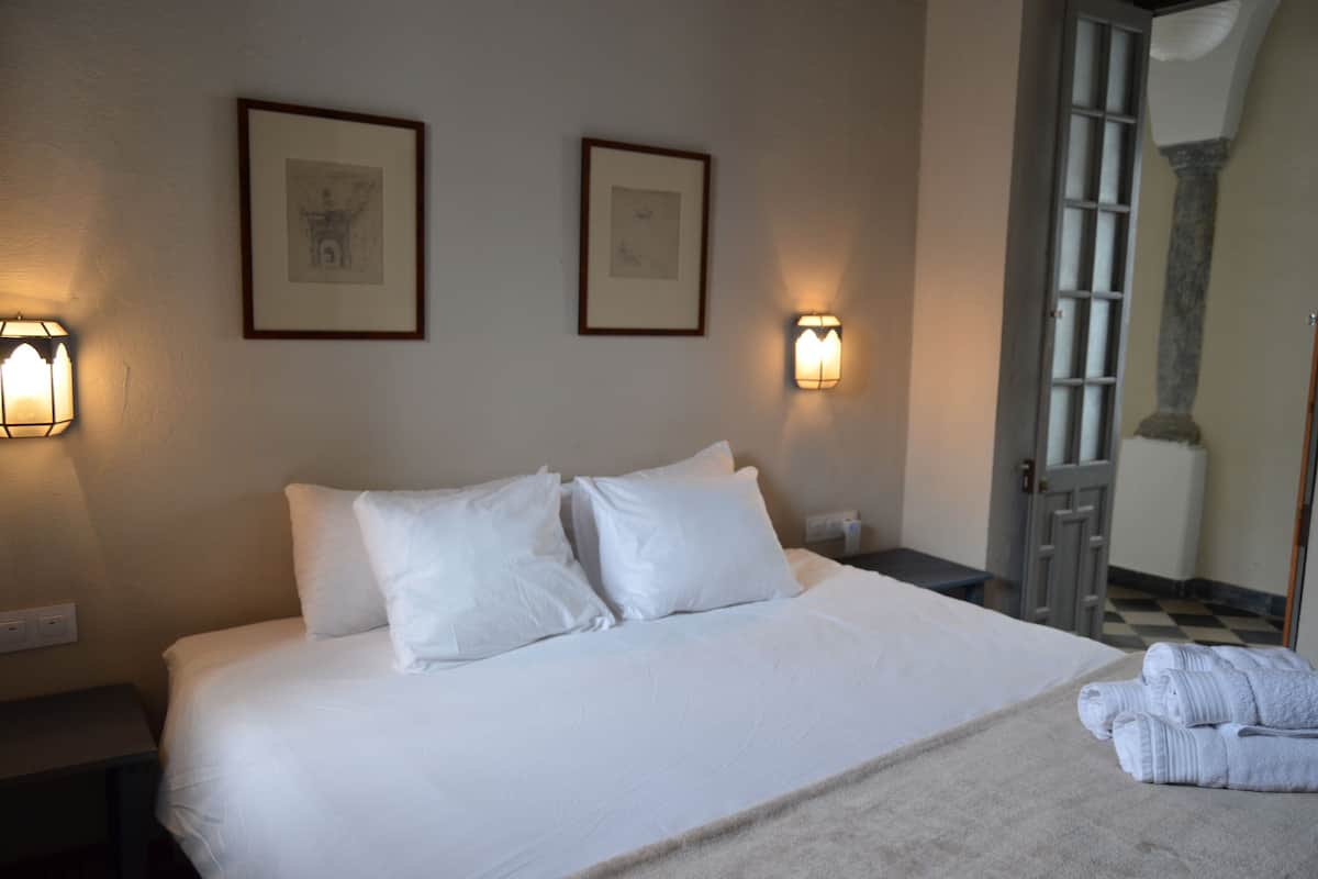 A neatly made bed with white linens, two framed pictures on the wall, and a pair of folded towels on the bed.