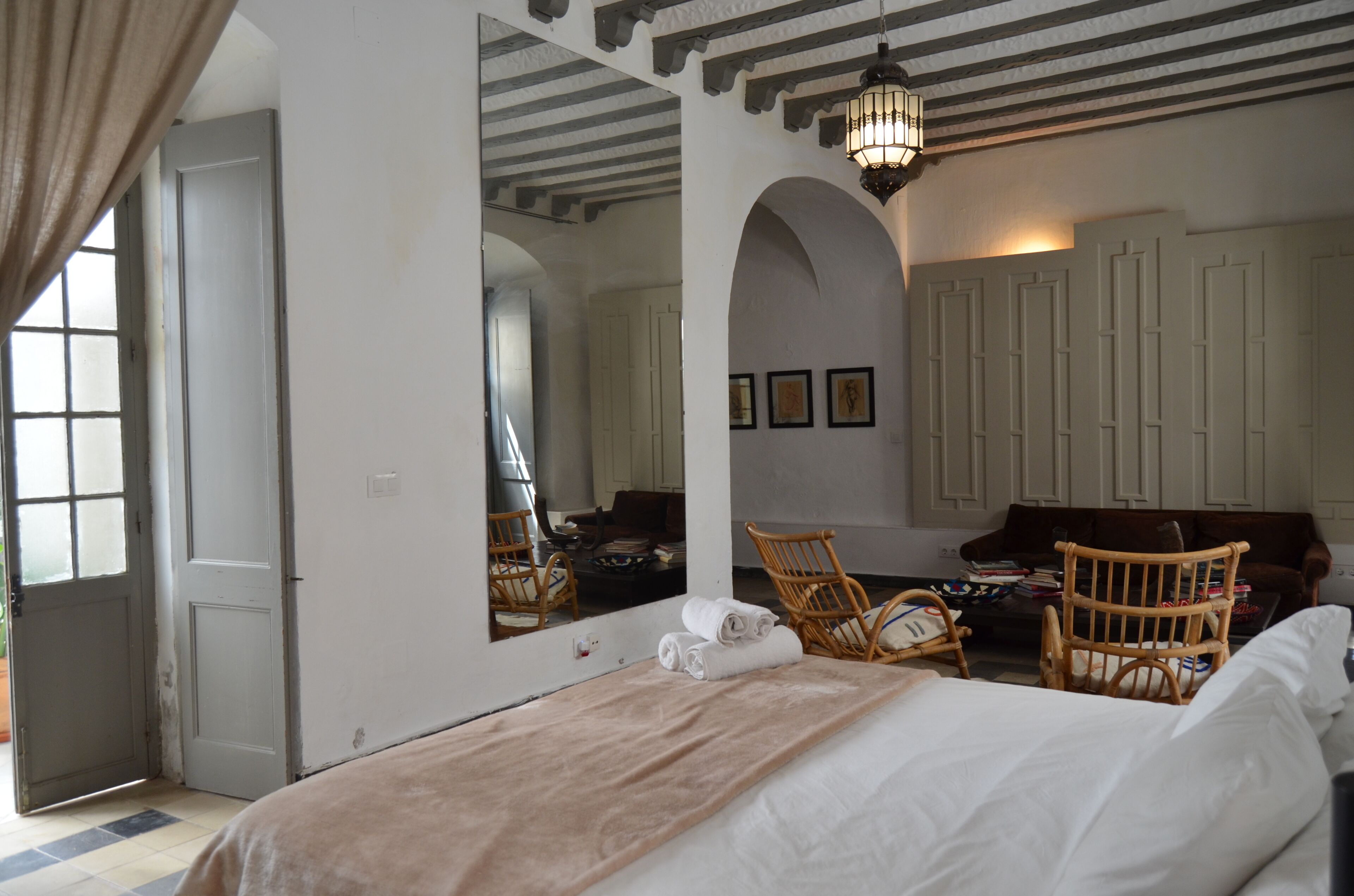 Un dormitorio con una cama grande, dos sillones de mimbre, un espejo y un armario.