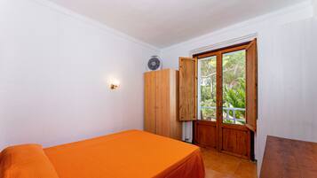 Una habitación con una cama, un armario de madera, un ventilador y una puerta que da a un área exterior.