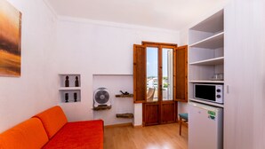 A compact living space with a sofa, a fan, a microwave, and a refrigerator. - Hostal Residencia San Francisco (Felanitx)
