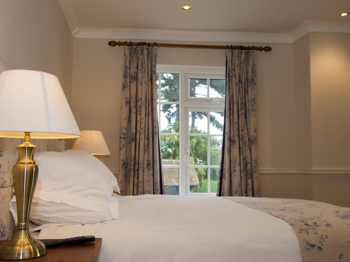 A hotel room with a bed, two lamps, a remote control, and a window with curtains.
