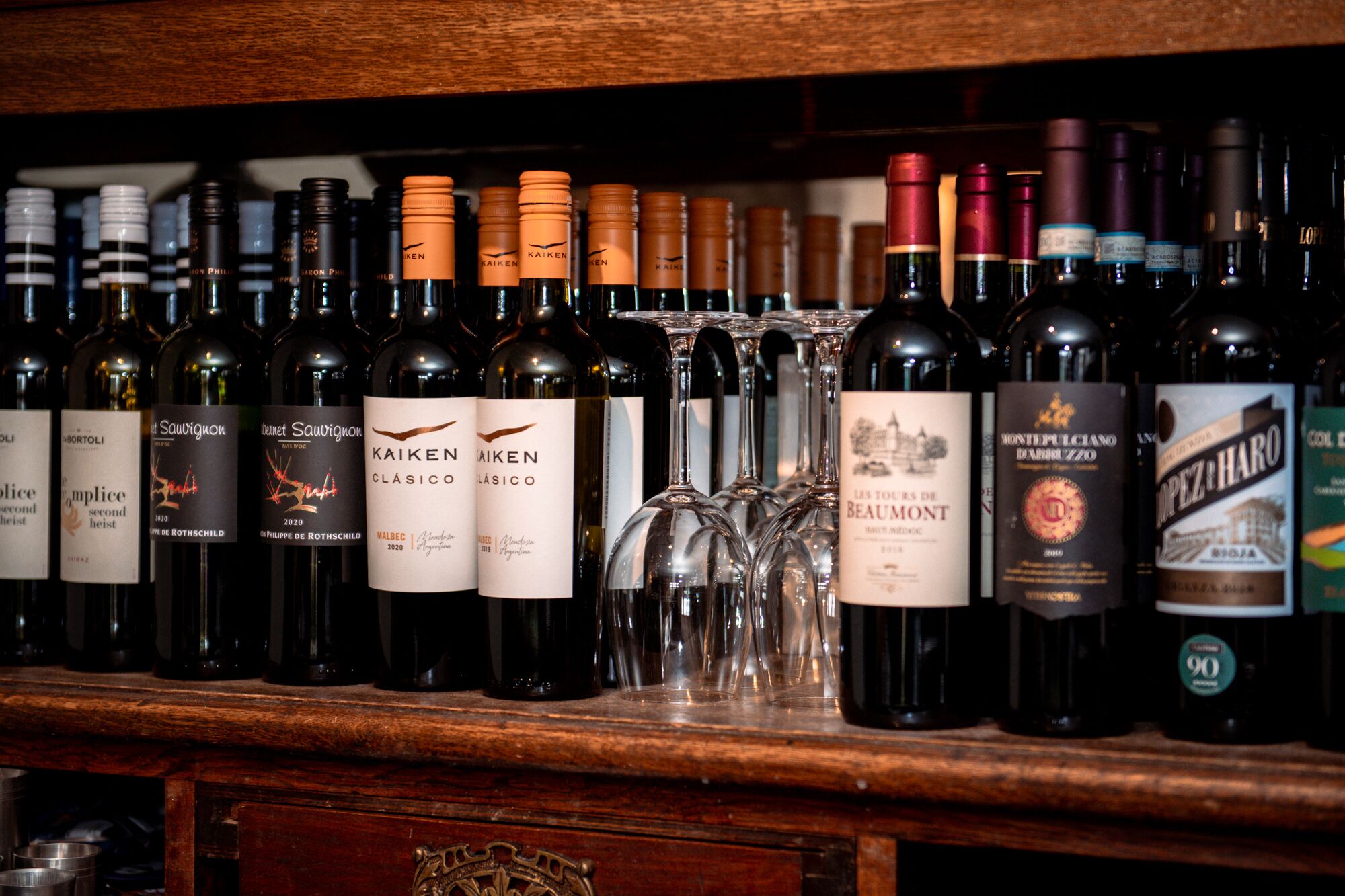 Variedad de botellas de vino y copas sobre un estante de madera.