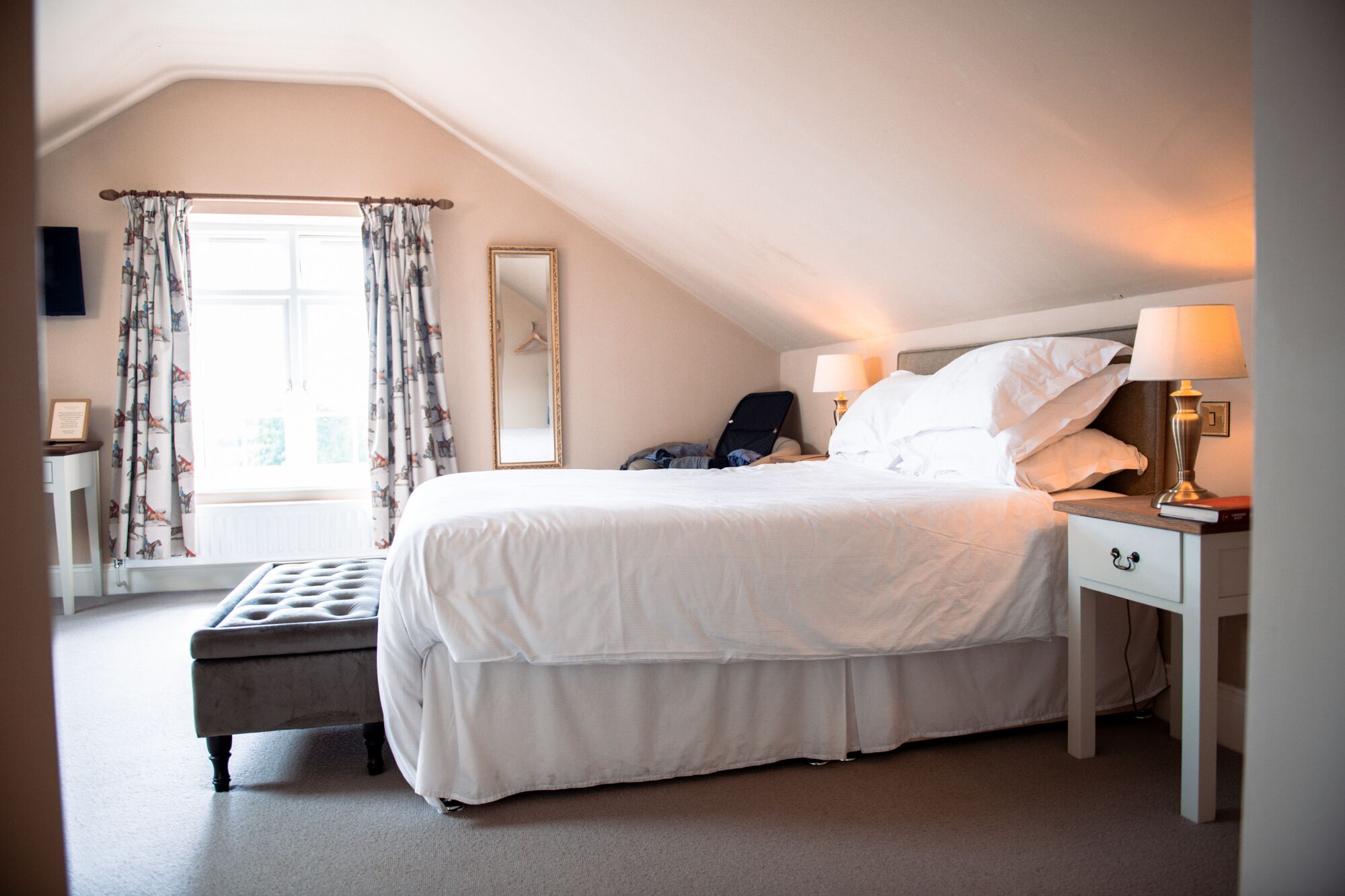 A neatly arranged bedroom with a large bed, bedside tables, a chair, and a window with curtains.