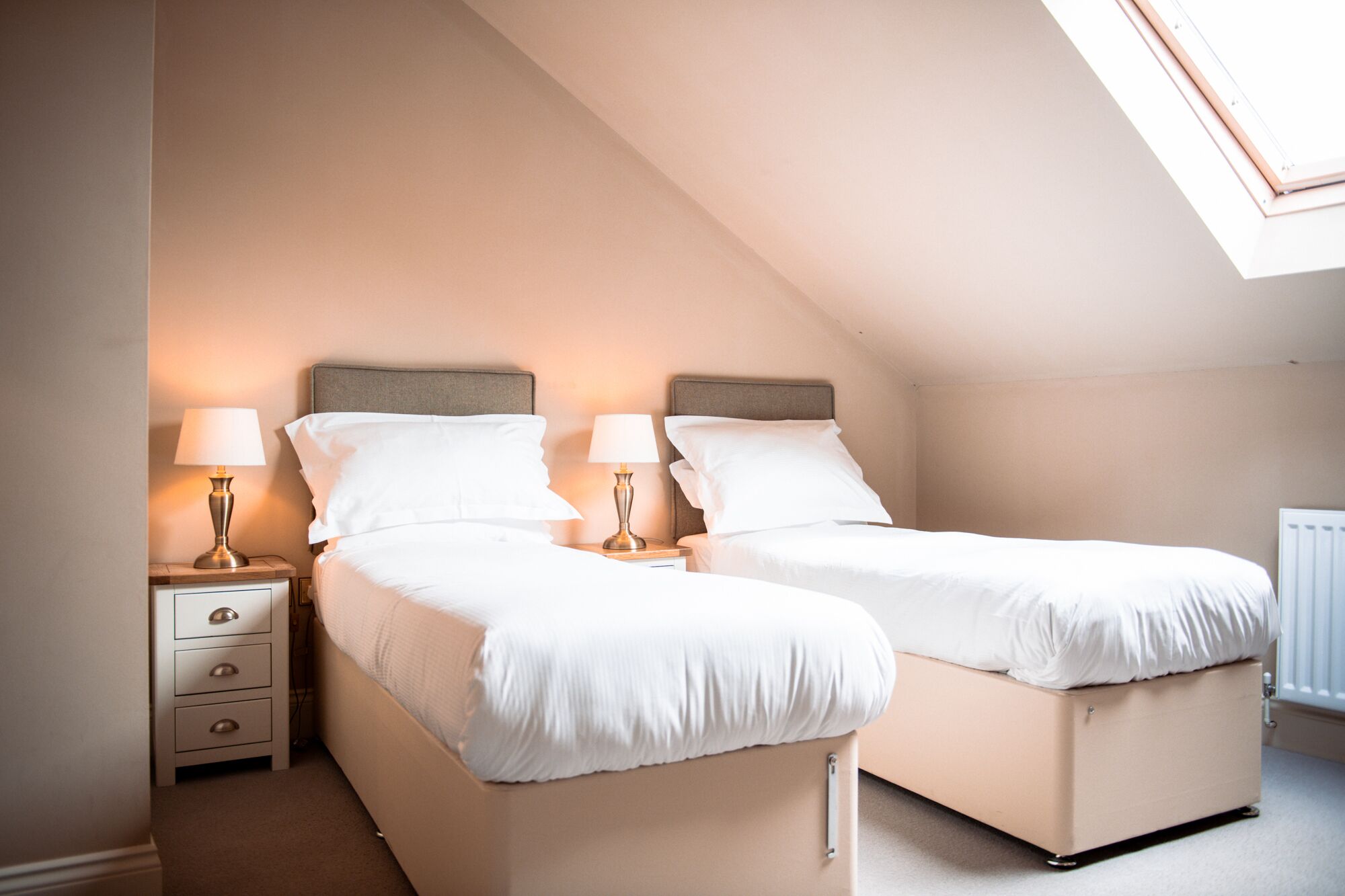 A twin room with two beds, bedside tables, lamps, and a radiator.