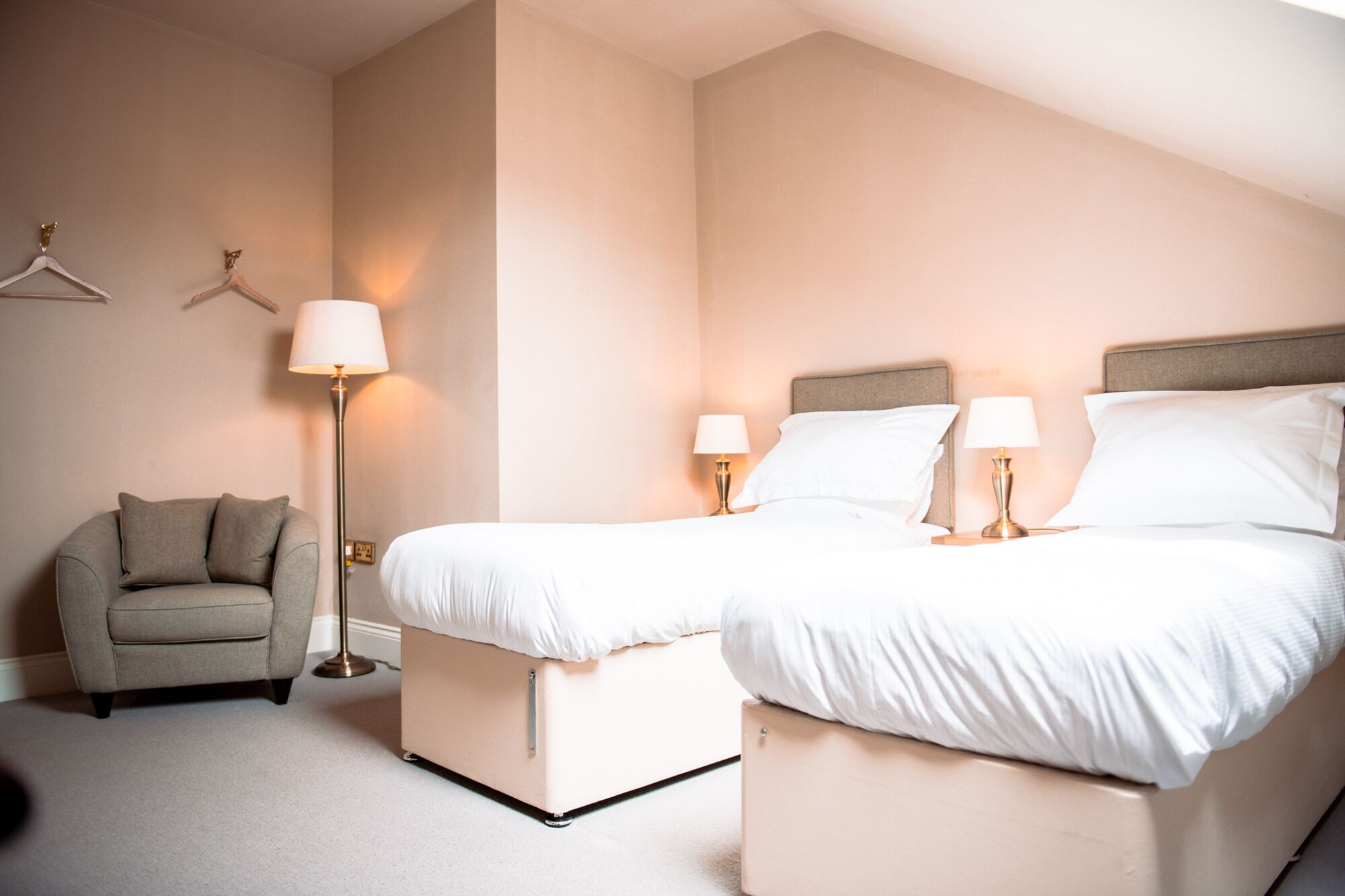 A hotel room with two beds, a chair, and two bedside lamps.