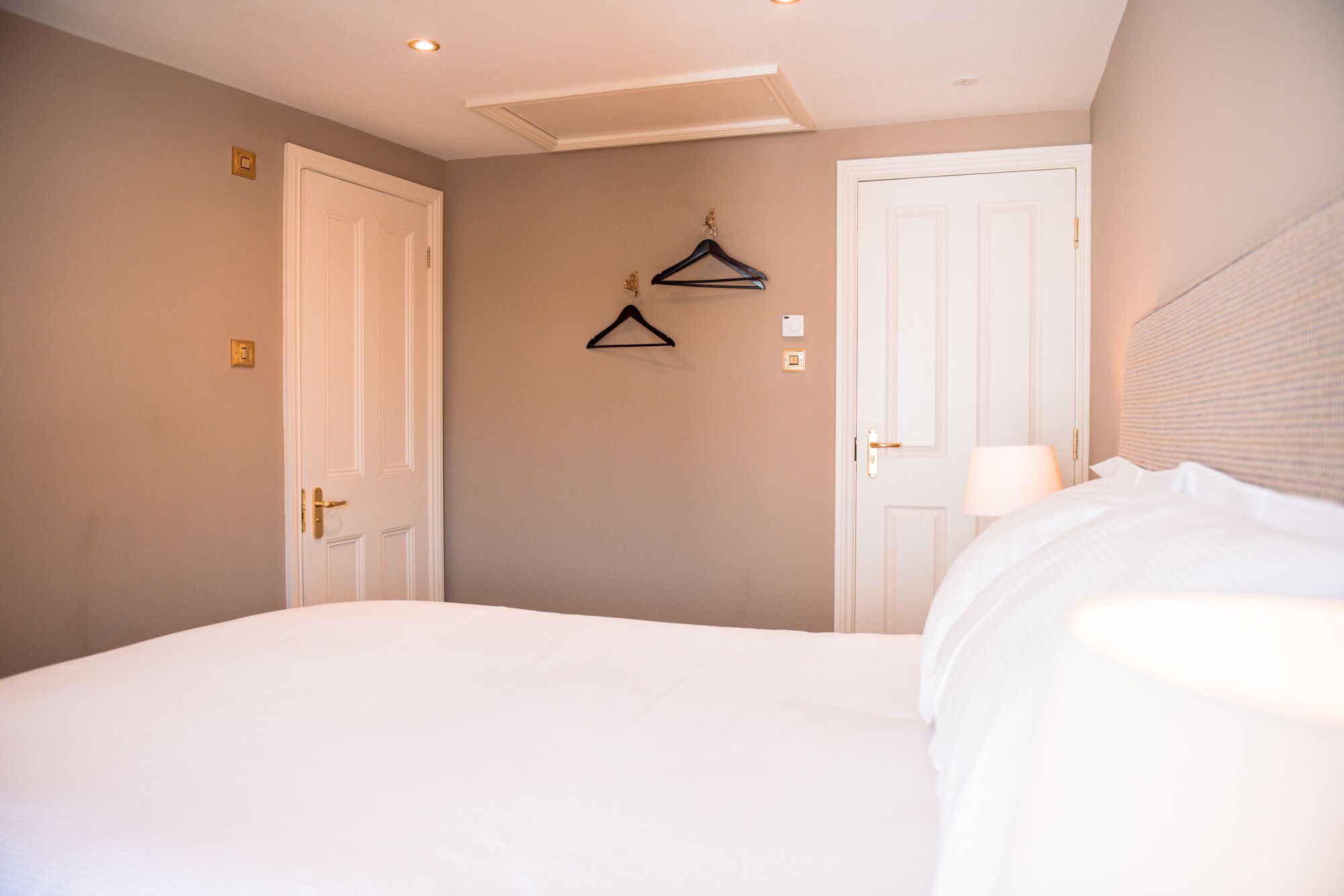 A bedroom with a bed, two doors, a wall-mounted light, and a hanging coat rack.