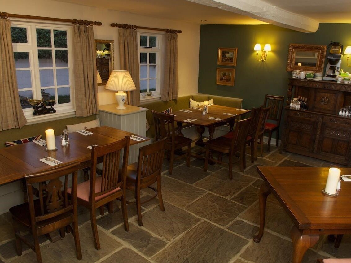 A dining area with wooden tables and chairs, a lamp, and a cabinet with a mirror and framed pictures.