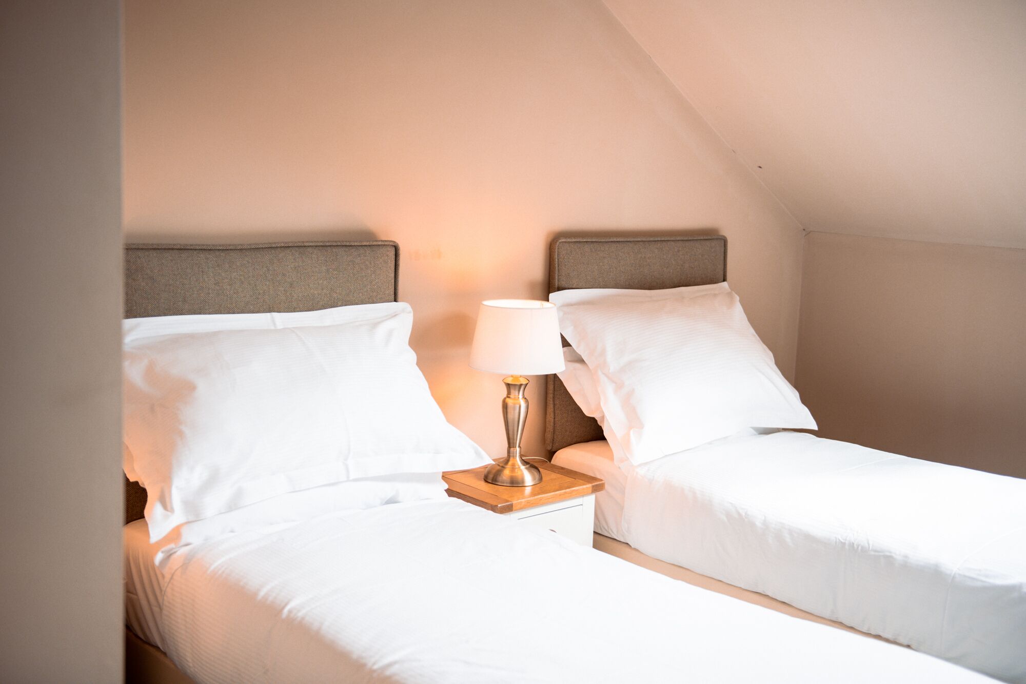 Ein Doppelzimmer mit zwei Betten, einem Nachttisch mit Lampe und einer schrägen Decke.