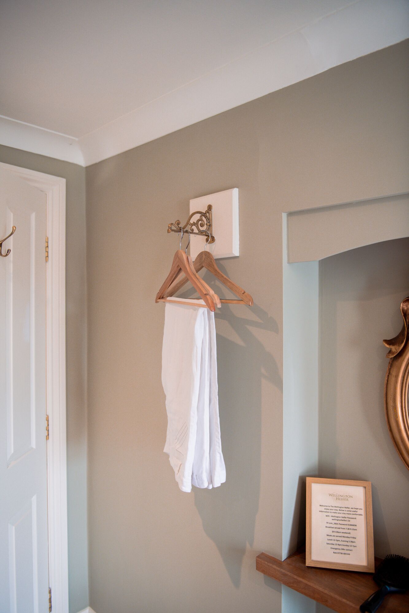 A room with a wooden hanger holding a white garment, a framed welcome sign, and a framed menu on a shelf.