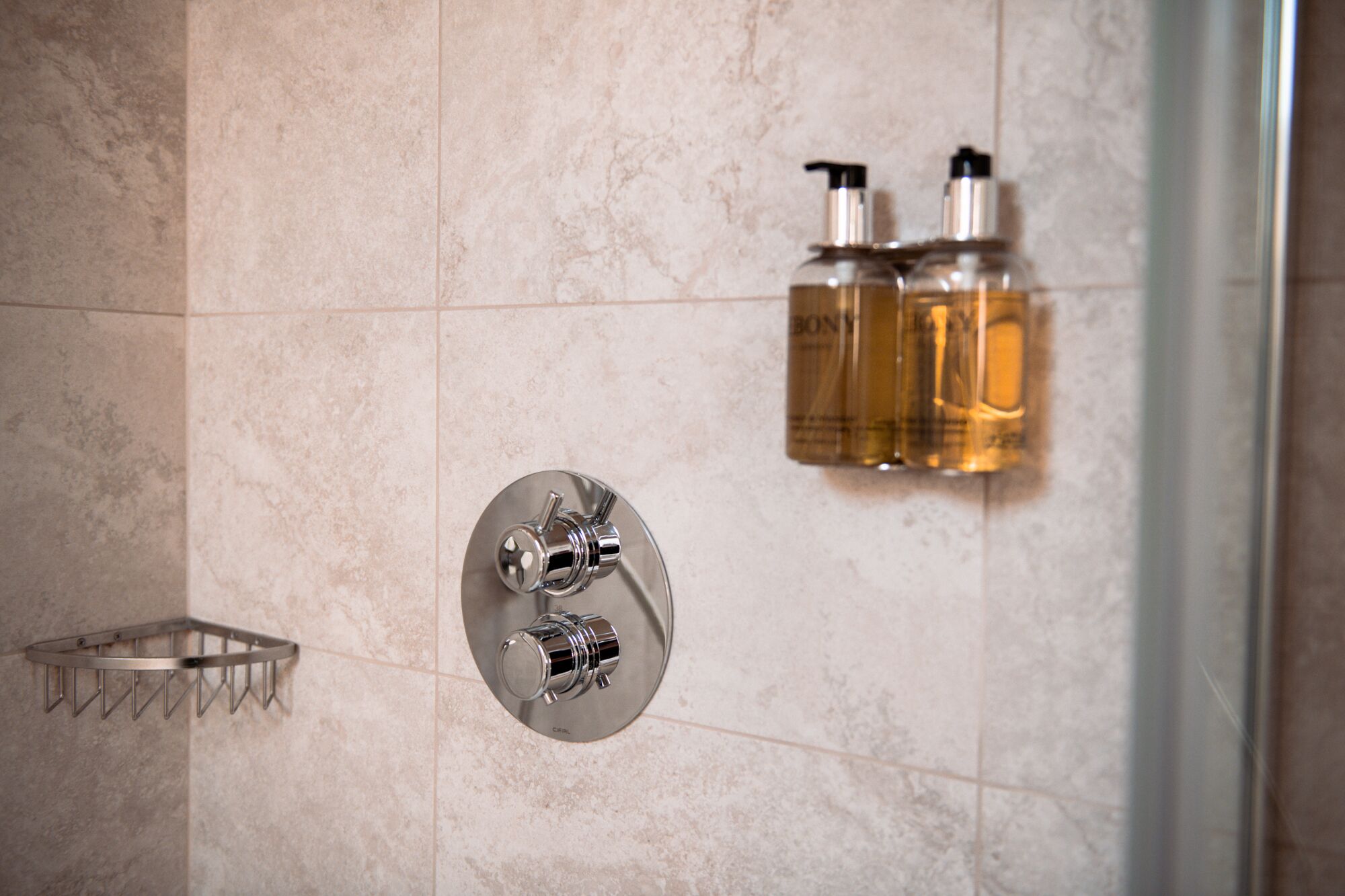 A bathroom with a shower, a towel rack, and two bottles of liquid soap.