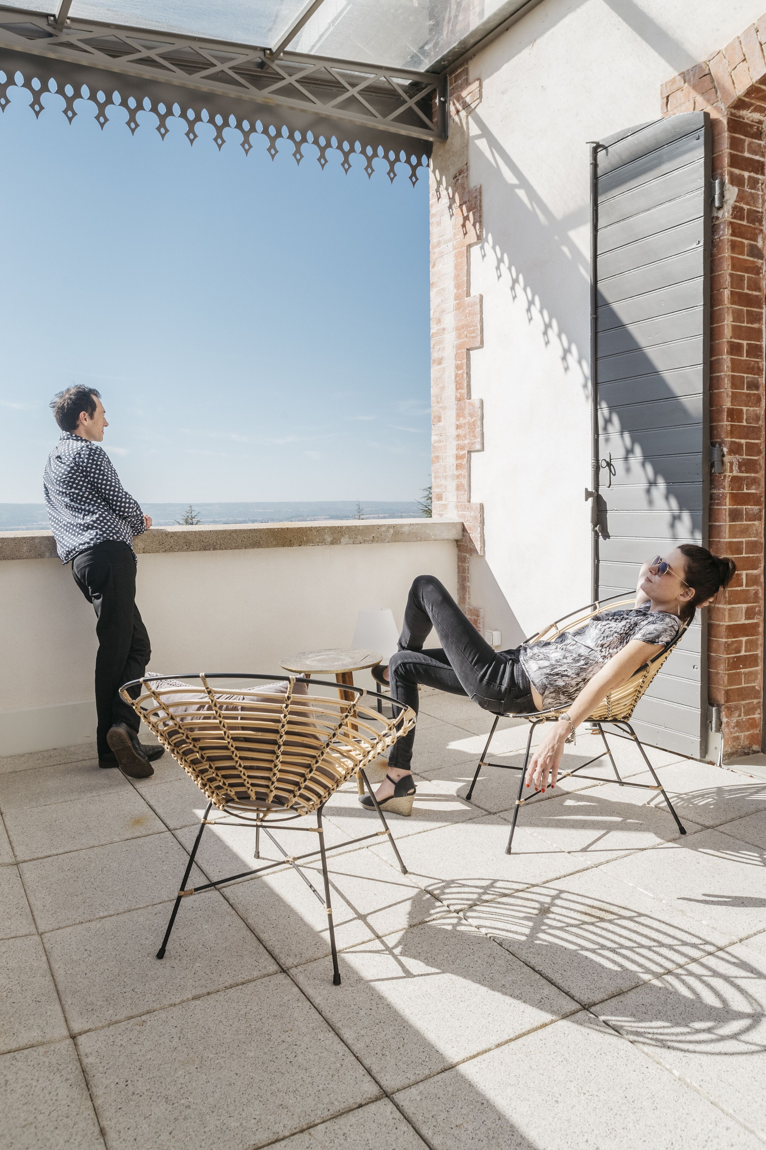 A balcony with a wicker chair and a table, a brick wall, and a metal gate.