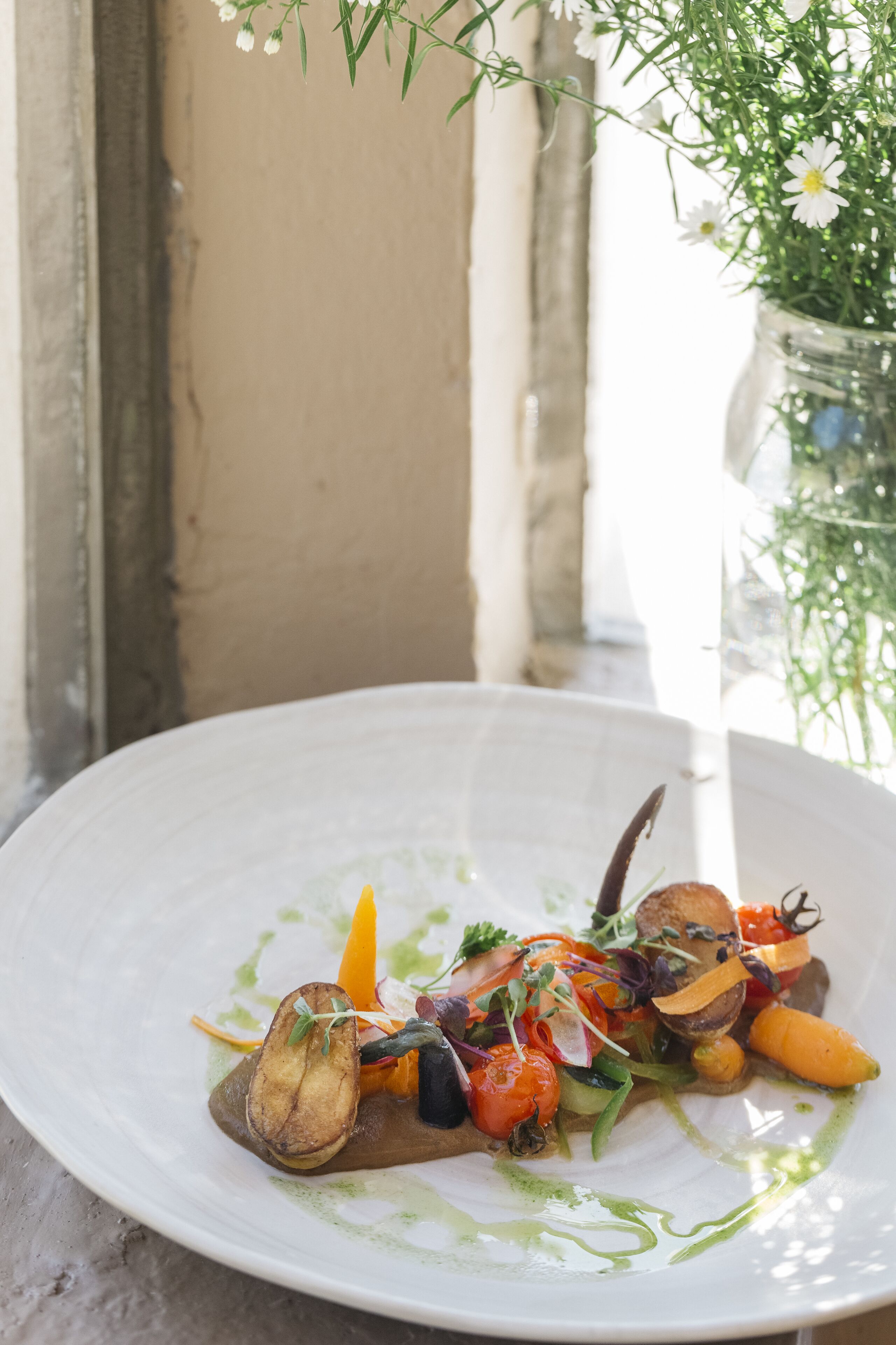 A white plate with a variety of vegetables and a green sauce, placed on an outdoor table.