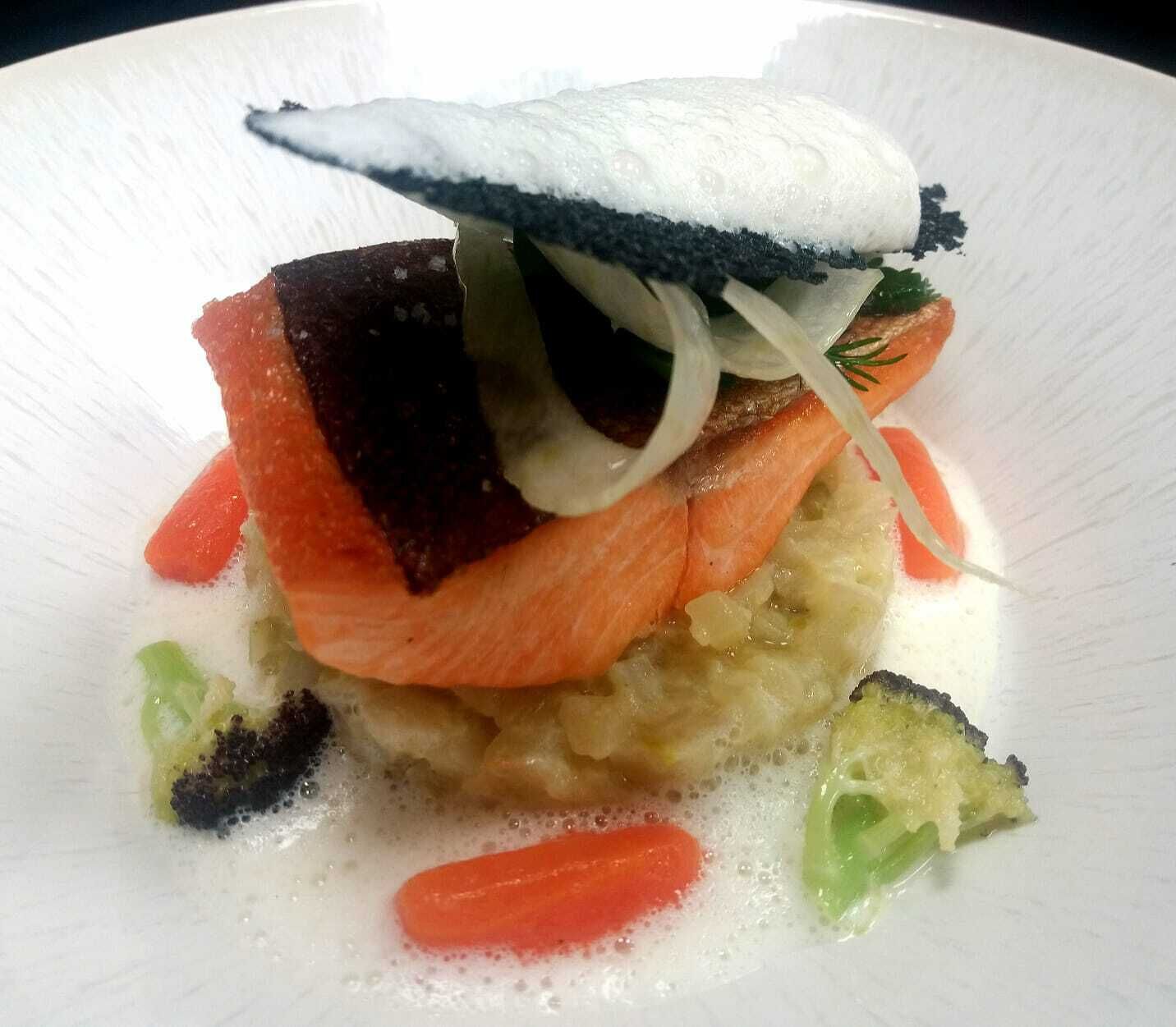 Une assiette blanche contenant un plat composé de saumon, de légumes et d’une sauce blanche.