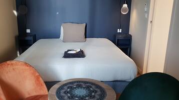A bedroom with a bed, a bedside table, a chair, and a small table with a decorative item.