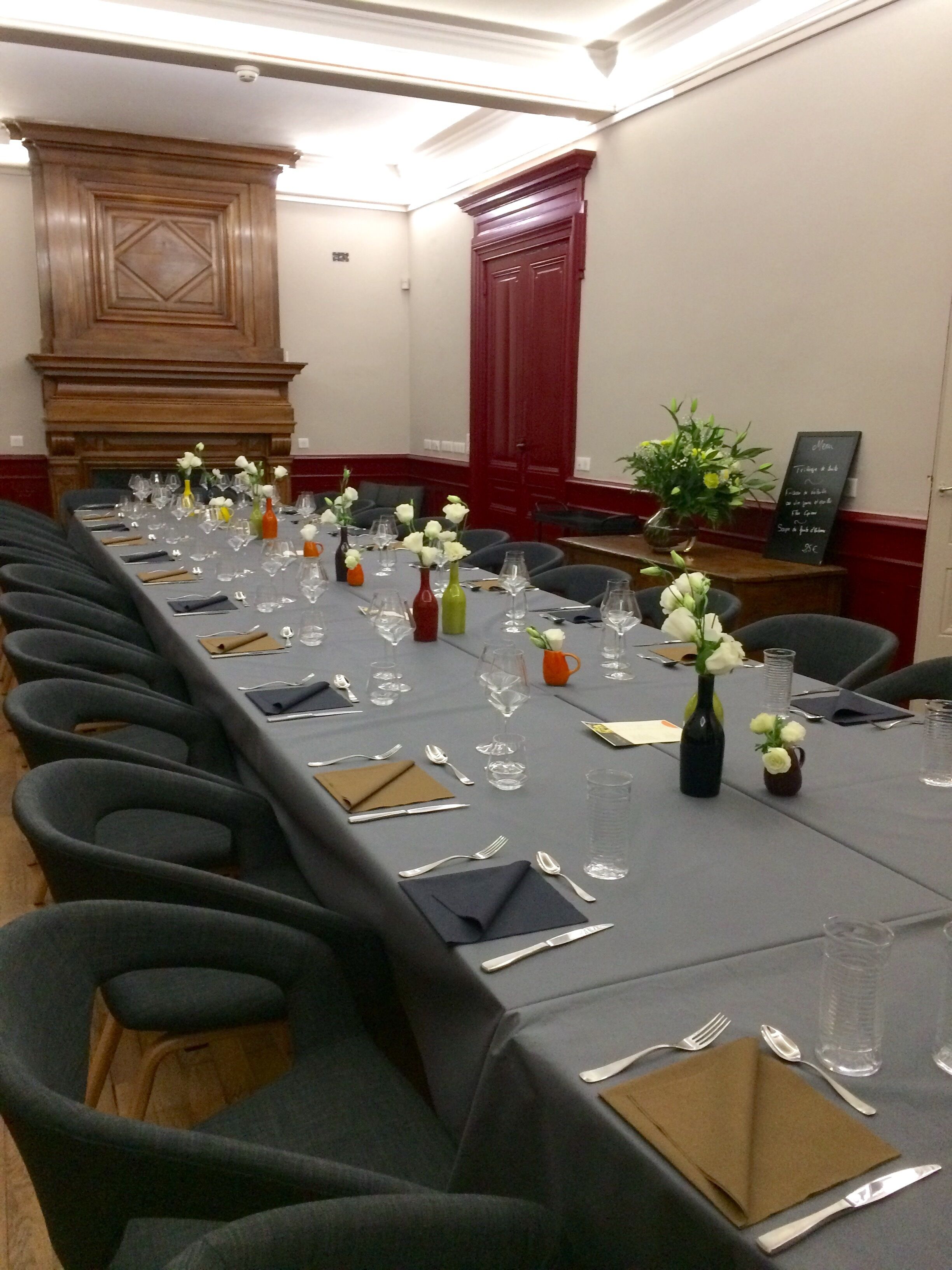 Une salle de conférence avec une longue table préparée pour une réunion, équipée de chaises, de verres à eau et agrémentée de compositions florales.
