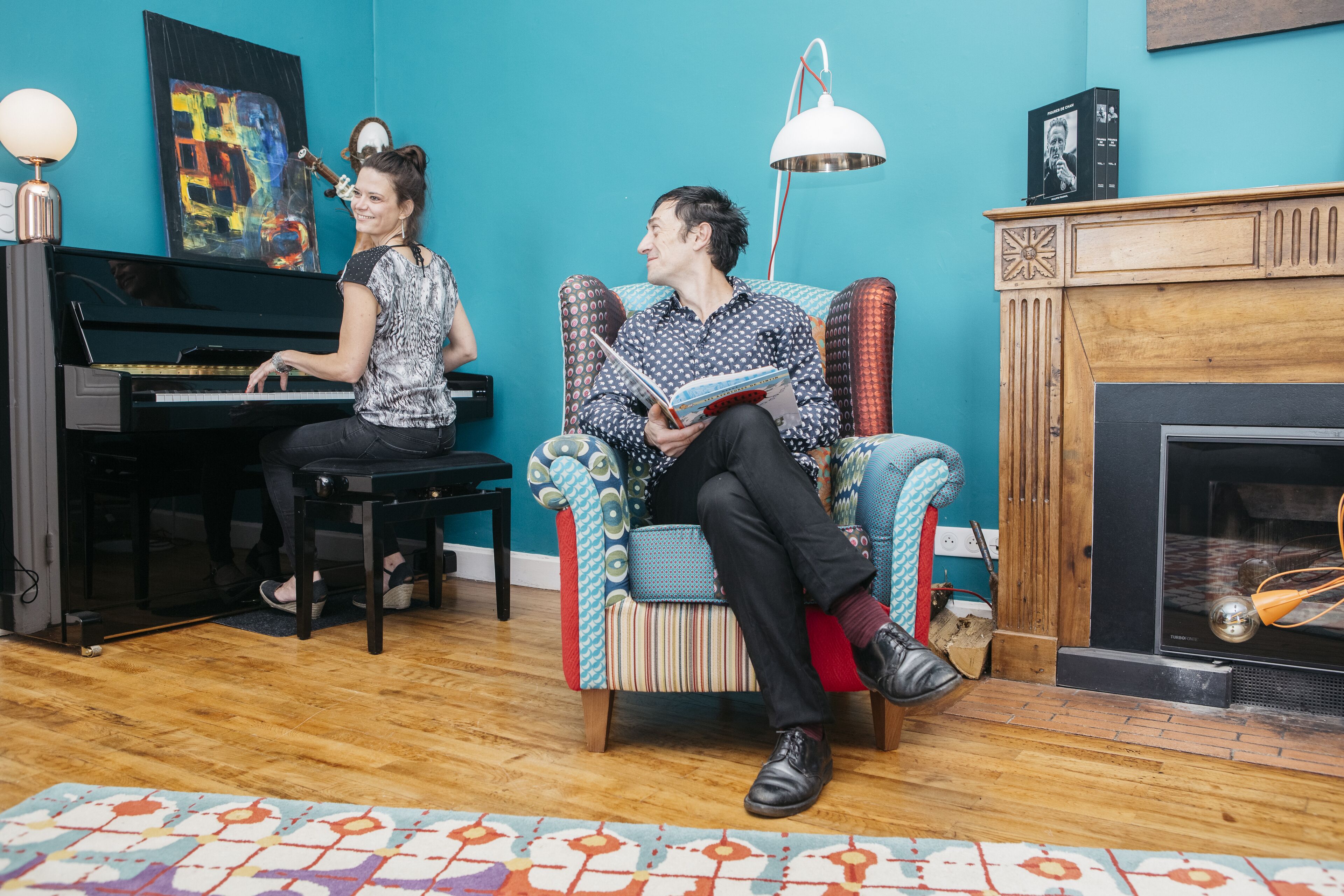 A room with a piano, a patterned armchair, a fireplace, and a colorful rug.