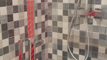 Une douche avec une porte en verre et un mur recouvert de carreaux à motifs géométriques.