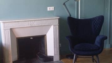 Una habitación con chimenea blanca, un sillón azul oscuro y una lámpara de pie.