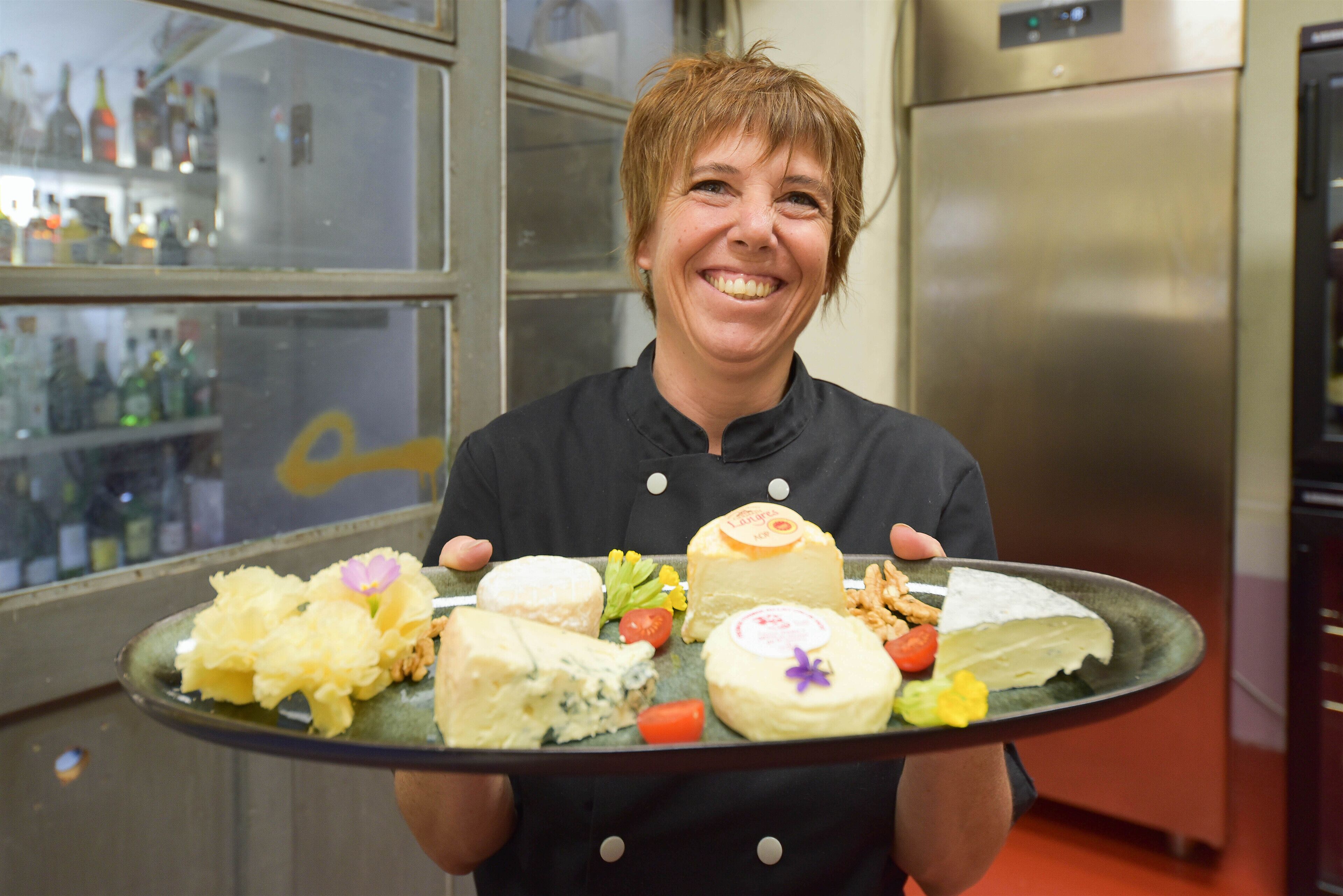 Una persona sosteniendo una bandeja con varios quesos y verduras.