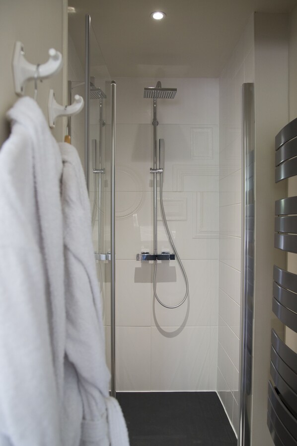 Un baño moderno con ducha de vidrio, toallero blanco y piso negro.